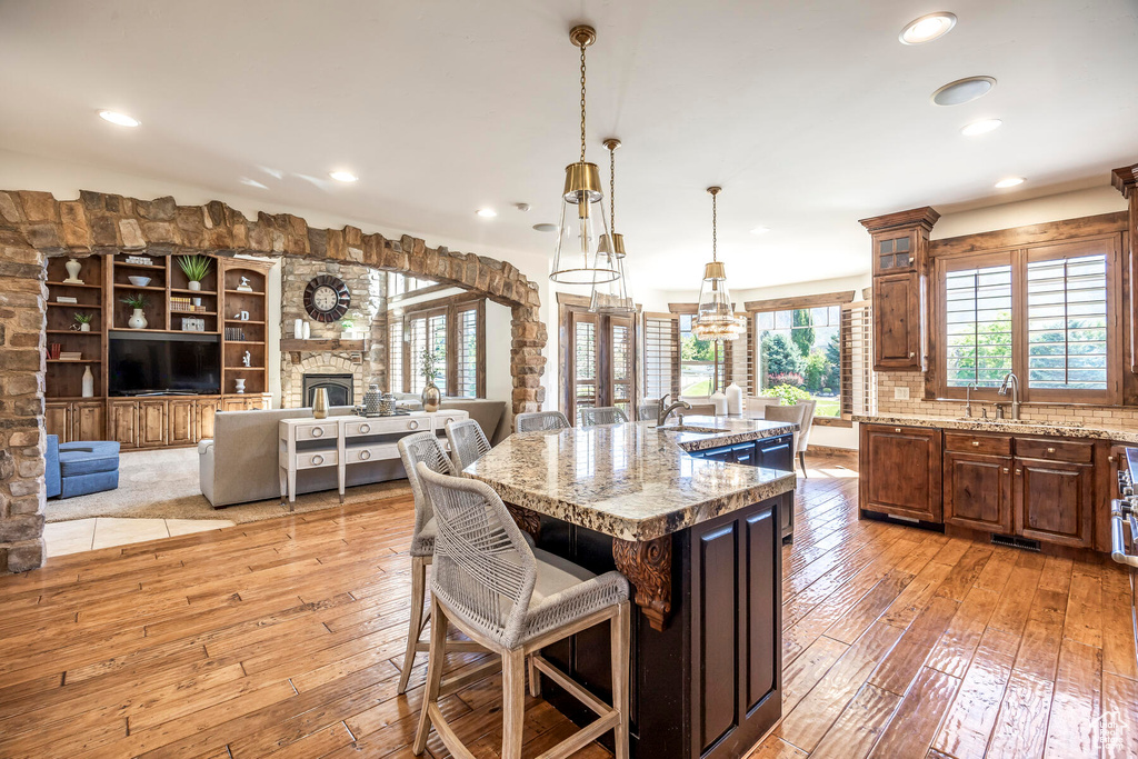 Kitchen with built in features, light wood-type flooring, pendant lighting, a fireplace, and a center island with sink