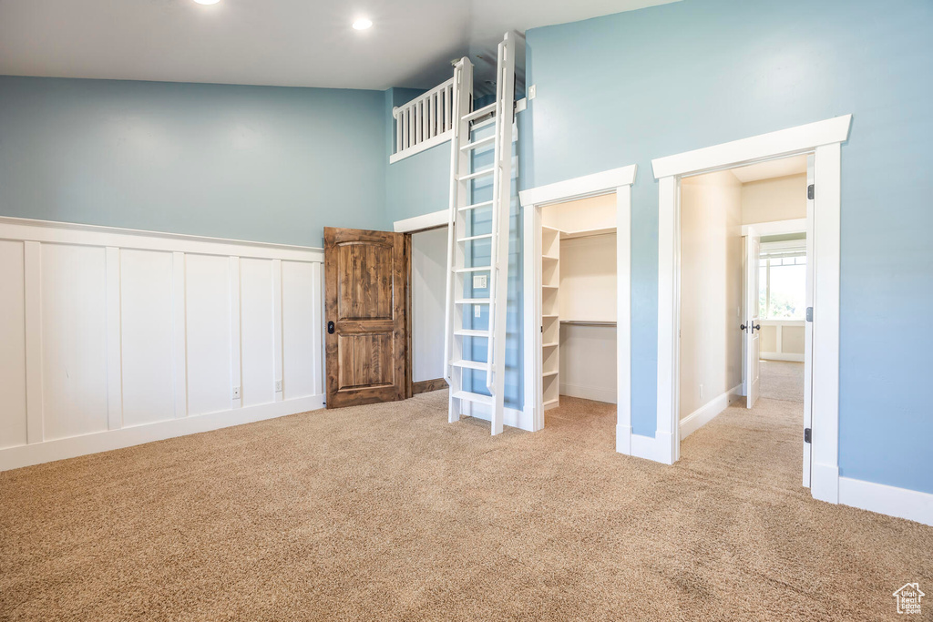 Interior space featuring a walk in closet, a closet, high vaulted ceiling, and light colored carpet