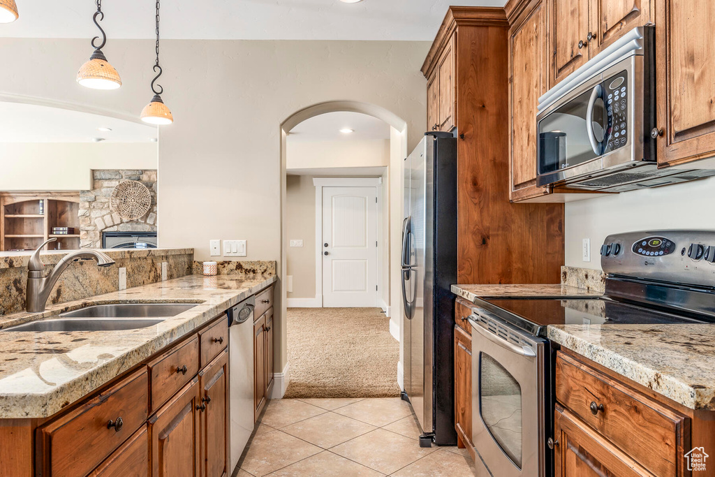 Kitchen featuring light stone counters, light tile patterned floors, sink, decorative light fixtures, and stainless steel appliances