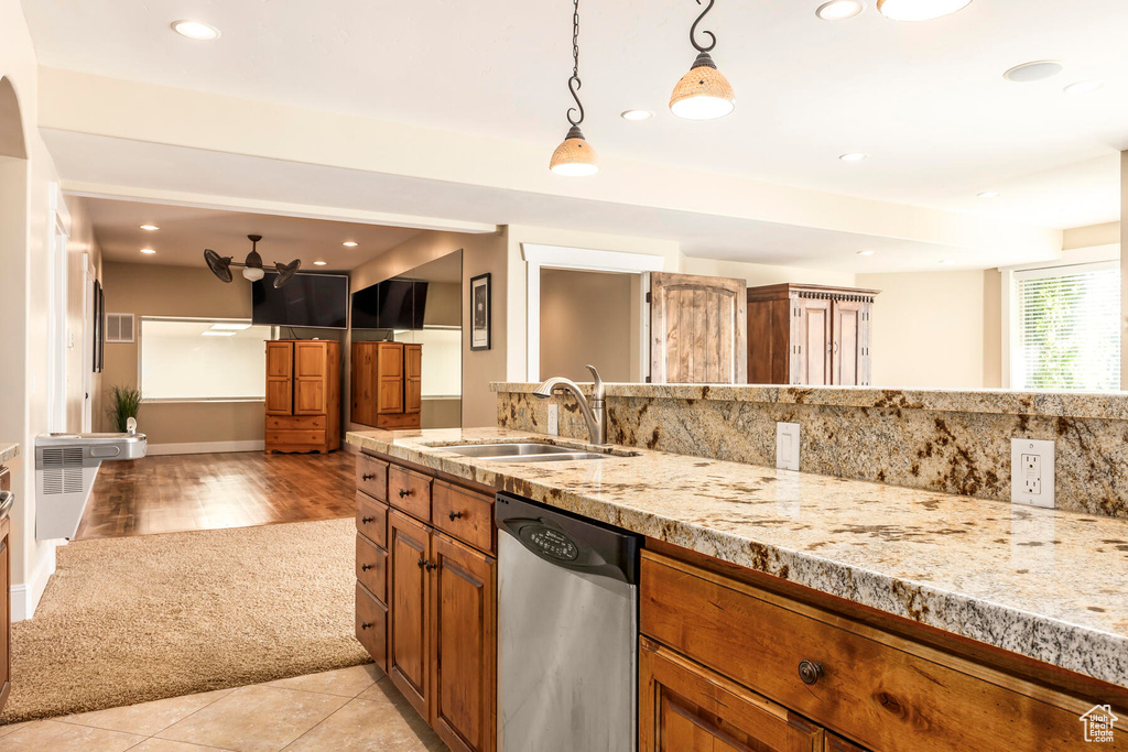 Kitchen featuring hanging light fixtures, dishwasher, light stone countertops, light tile patterned floors, and sink