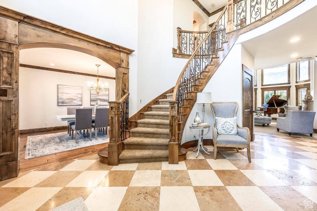 Stairs featuring hardwood / wood-style floors, a towering ceiling, crown molding, and a notable chandelier