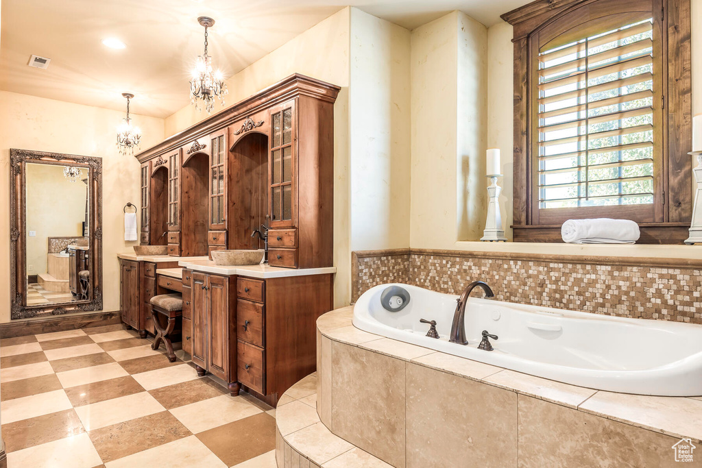 Bathroom with tile patterned flooring, an inviting chandelier, vanity, and tiled bath