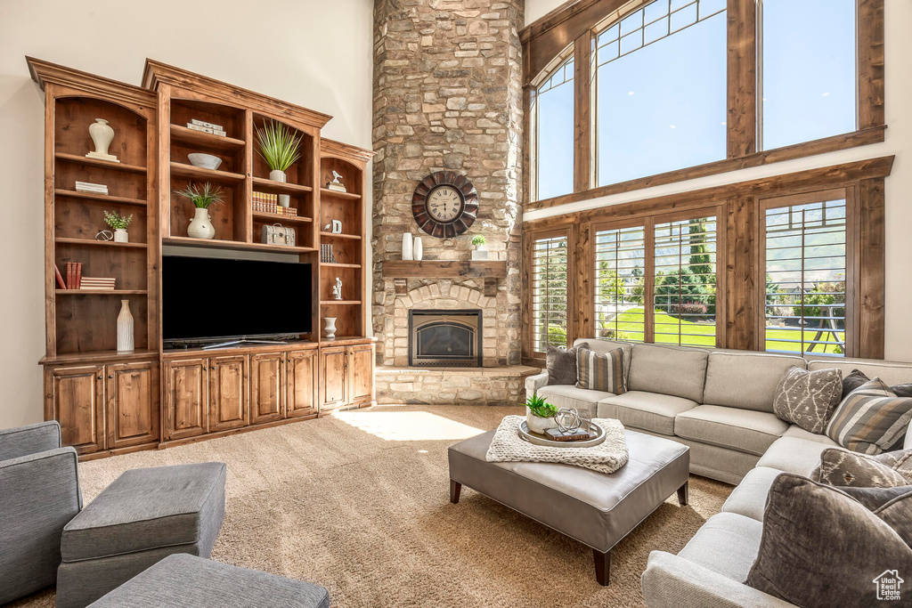 Living room with carpet, built in features, a high ceiling, and a stone fireplace