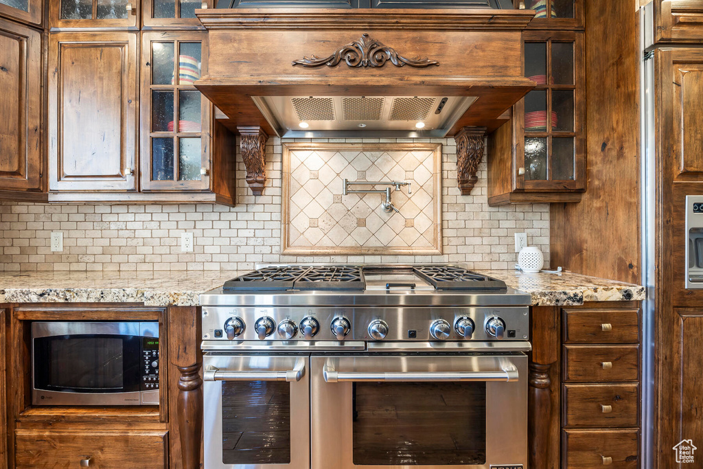 Kitchen featuring appliances with stainless steel finishes, light stone counters, wall chimney exhaust hood, and backsplash