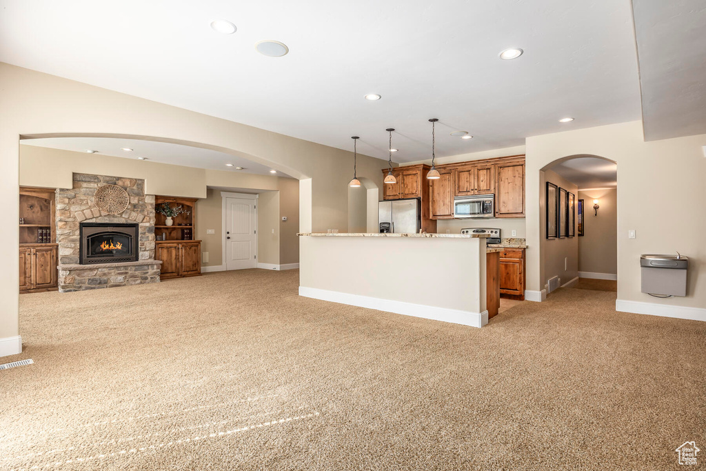 Kitchen featuring a fireplace, appliances with stainless steel finishes, a kitchen island, light carpet, and hanging light fixtures