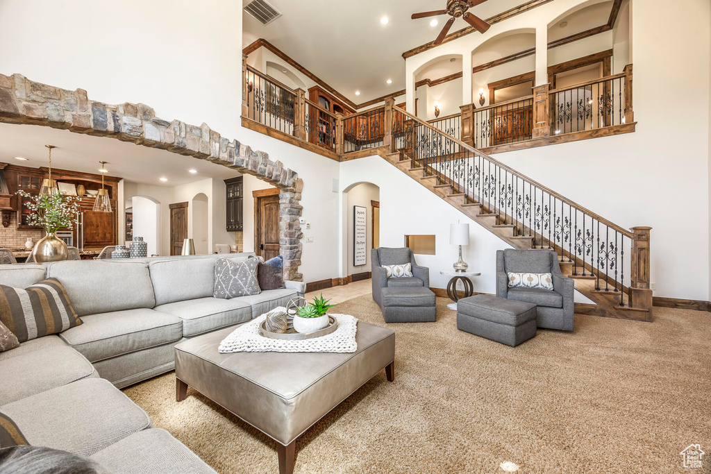 Living room with ceiling fan, a towering ceiling, and light colored carpet