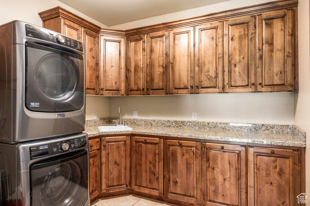 Kitchen featuring sink, stacked washer and dryer, light tile patterned floors, and light stone countertops