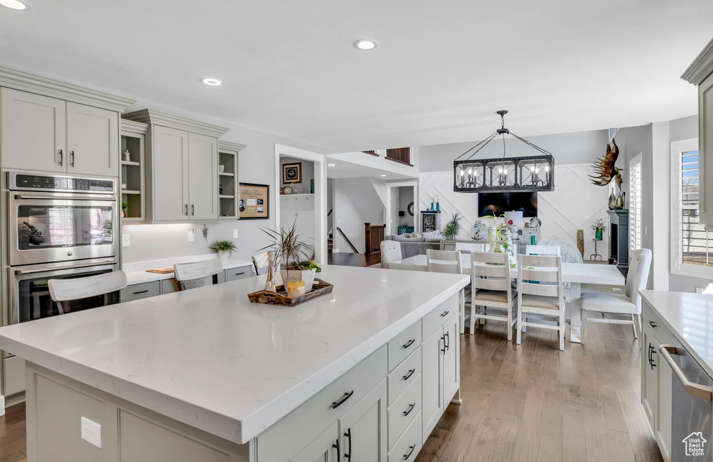 Kitchen with appliances with stainless steel finishes, a notable chandelier, light hardwood / wood-style floors, decorative light fixtures, and a center island