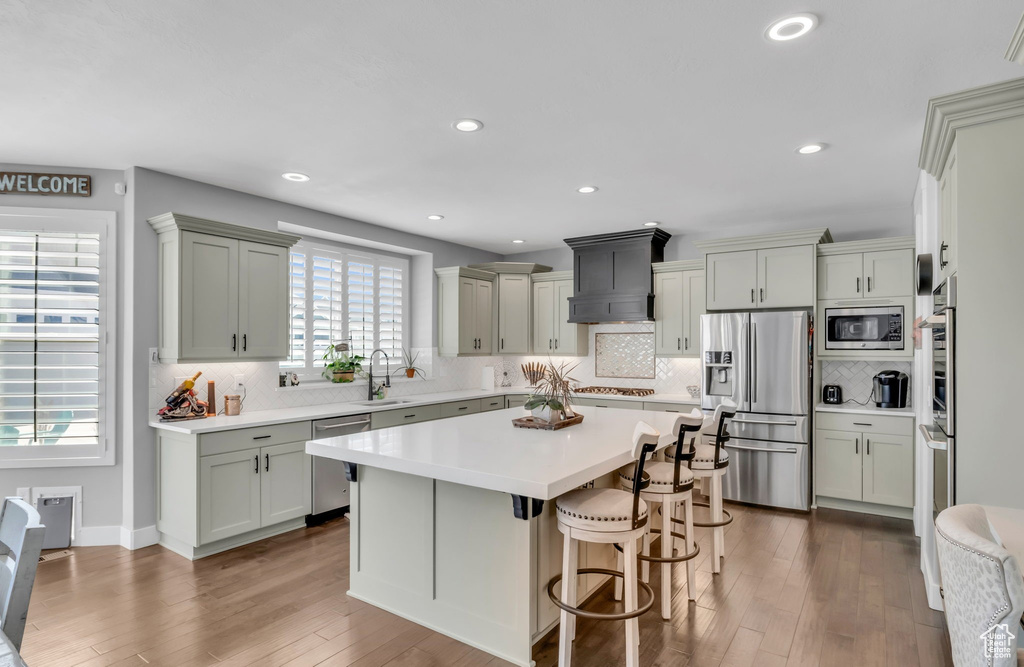 Kitchen featuring backsplash, custom exhaust hood, stainless steel appliances, hardwood / wood-style floors, and a breakfast bar area