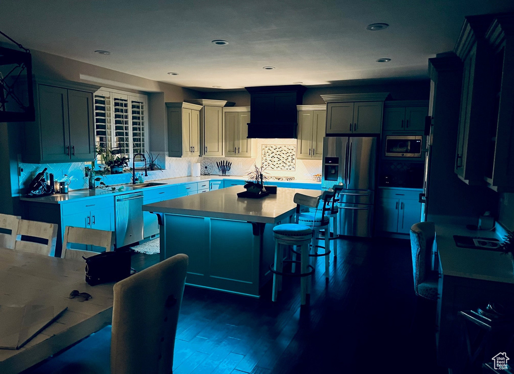 Kitchen with a kitchen island, a kitchen bar, dark wood-type flooring, backsplash, and stainless steel appliances
