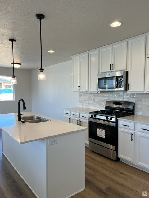 Kitchen featuring appliances with stainless steel finishes, dark hardwood / wood-style floors, white cabinets, sink, and pendant lighting