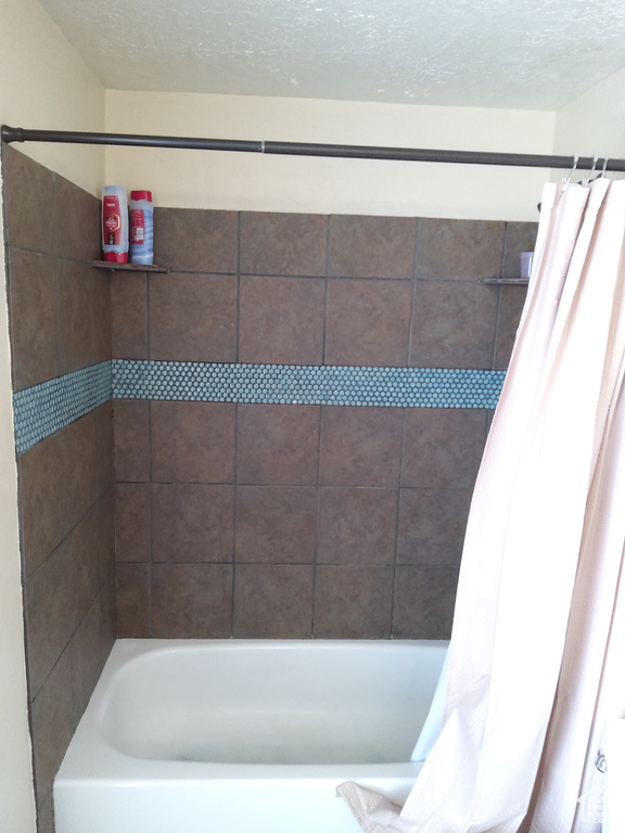 Bathroom with a textured ceiling and shower / tub combo