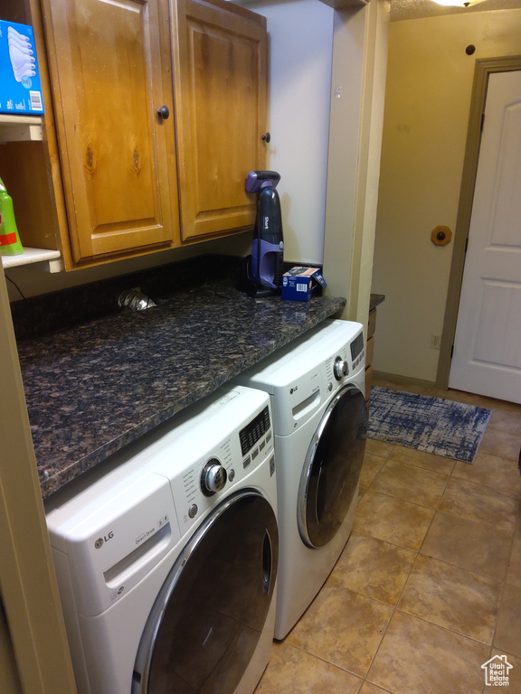 Laundry area featuring washing machine and dryer, light tile floors, and cabinets