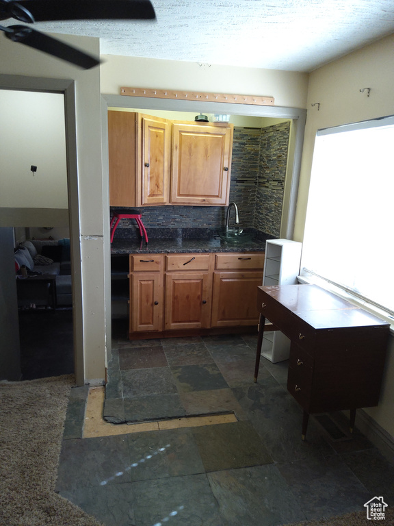 Kitchen featuring ceiling fan, sink, dark stone countertops, backsplash, and dark tile floors