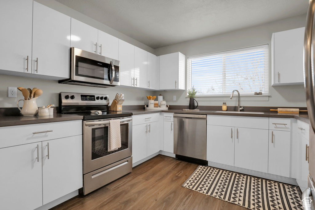 Kitchen featuring white cabinets, stainless steel appliances, sink, and hardwood / wood-style floors