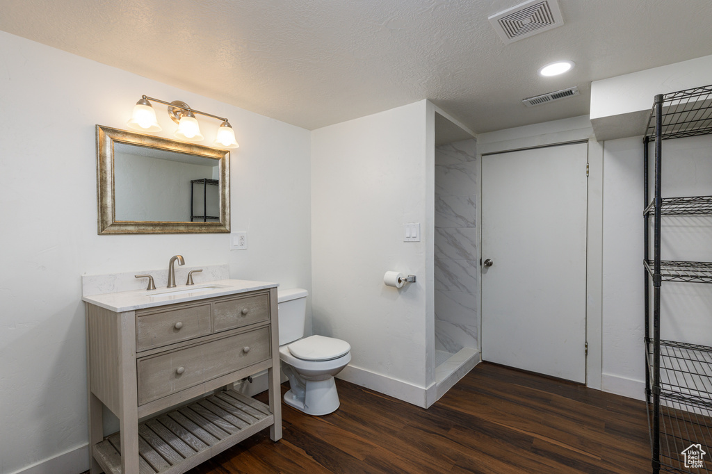Bathroom featuring hardwood / wood-style floors, a shower, a textured ceiling, toilet, and vanity