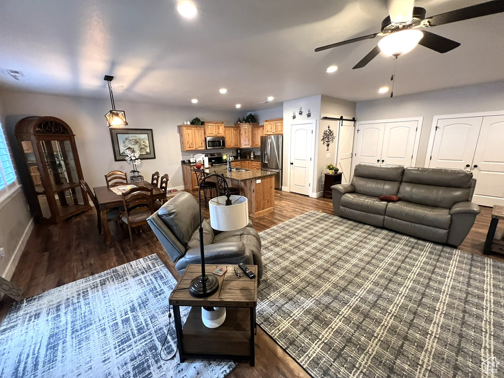 Living room featuring dark wood-type flooring, a barn door, sink, and ceiling fan