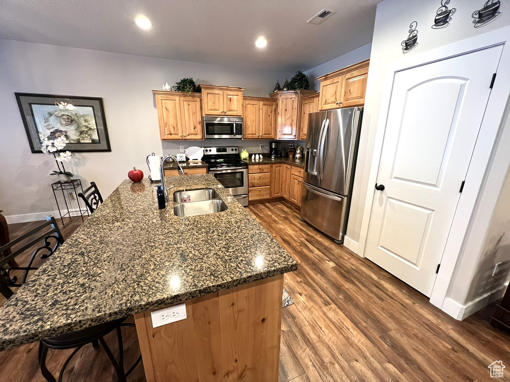 Kitchen with a center island with sink, stainless steel appliances, dark hardwood / wood-style floors, sink, and a breakfast bar