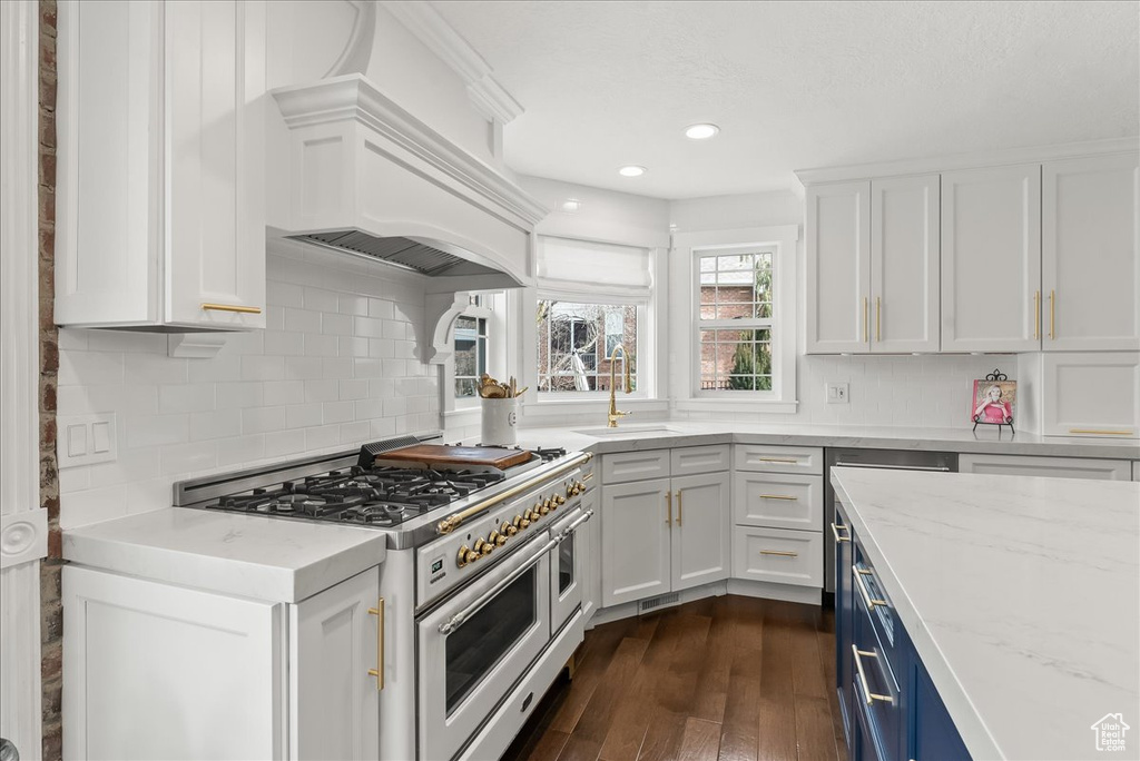 Kitchen with tasteful backsplash, white cabinets, dark hardwood / wood-style floors, range with two ovens, and light stone countertops
