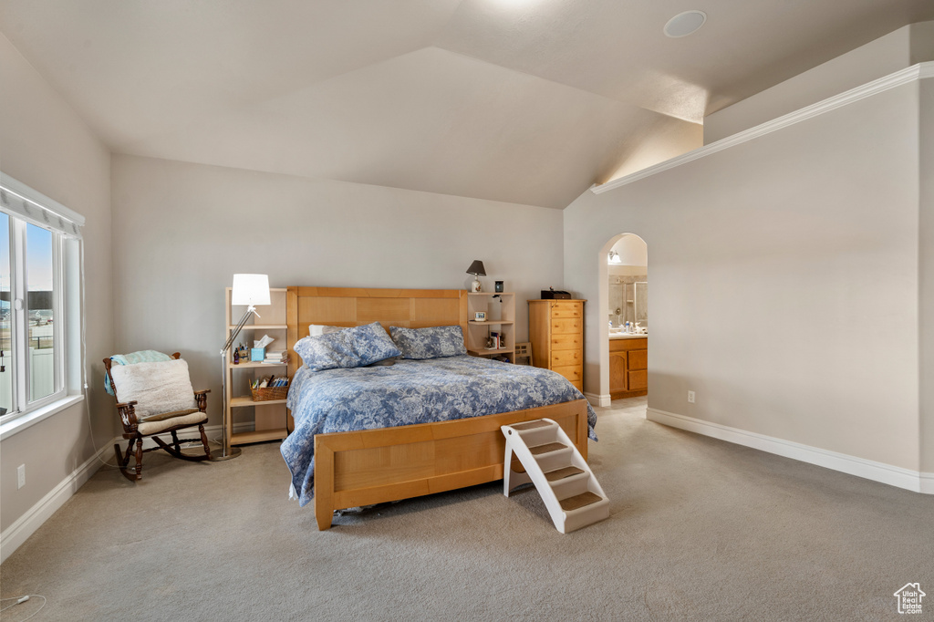 Bedroom featuring vaulted ceiling, light colored carpet, and ensuite bath