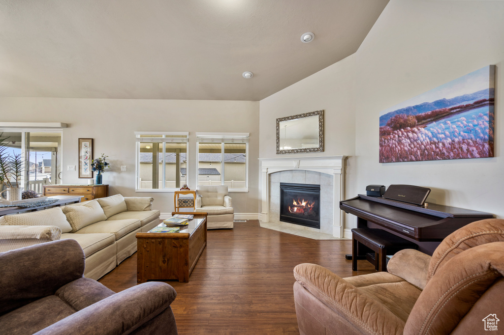 Living room with lofted ceiling, plenty of natural light, a tiled fireplace, and dark hardwood / wood-style flooring
