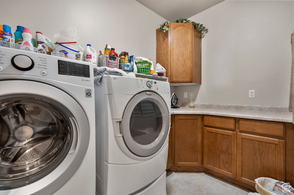 Clothes washing area featuring cabinets, light tile flooring, and washer and dryer