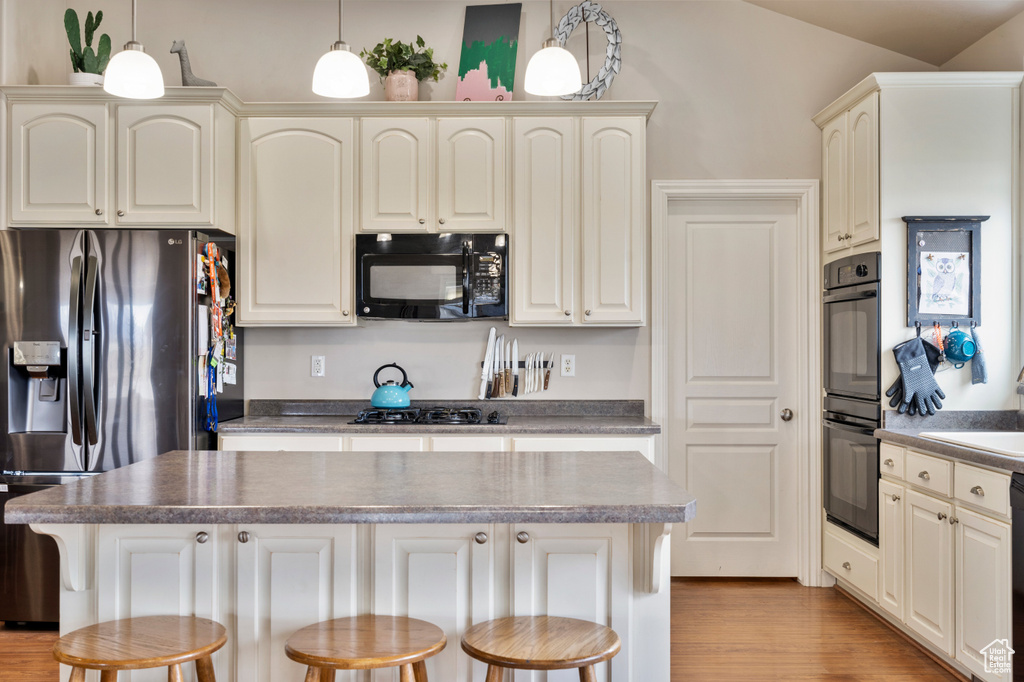 Kitchen featuring pendant lighting, a breakfast bar, black appliances, and light hardwood / wood-style floors
