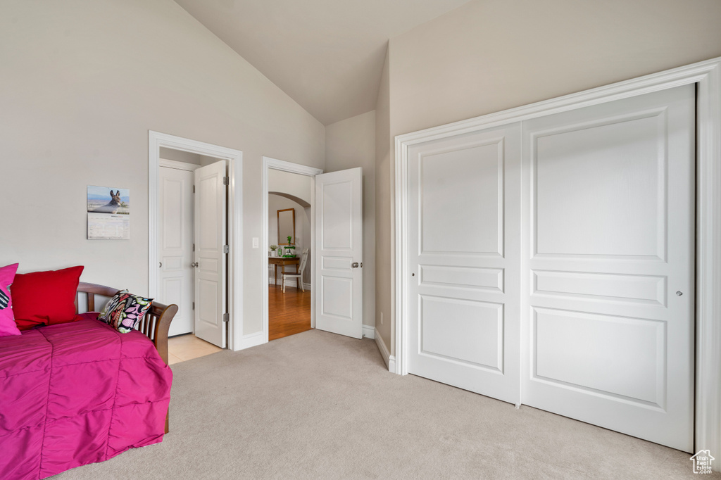 Bedroom featuring light carpet, a closet, and high vaulted ceiling