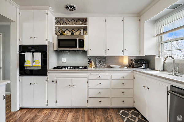 Kitchen featuring hardwood / wood-style flooring, tasteful backsplash, appliances with stainless steel finishes, white cabinets, and crown molding