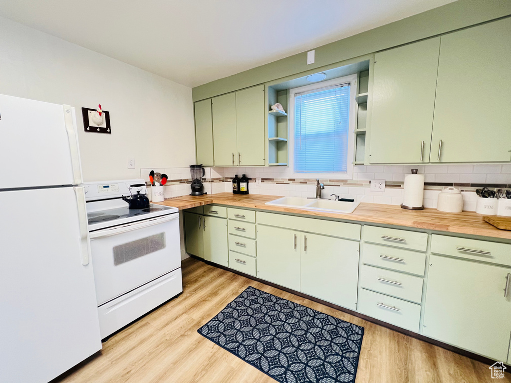 Kitchen with white appliances, sink, green cabinets, light wood-type flooring, and backsplash