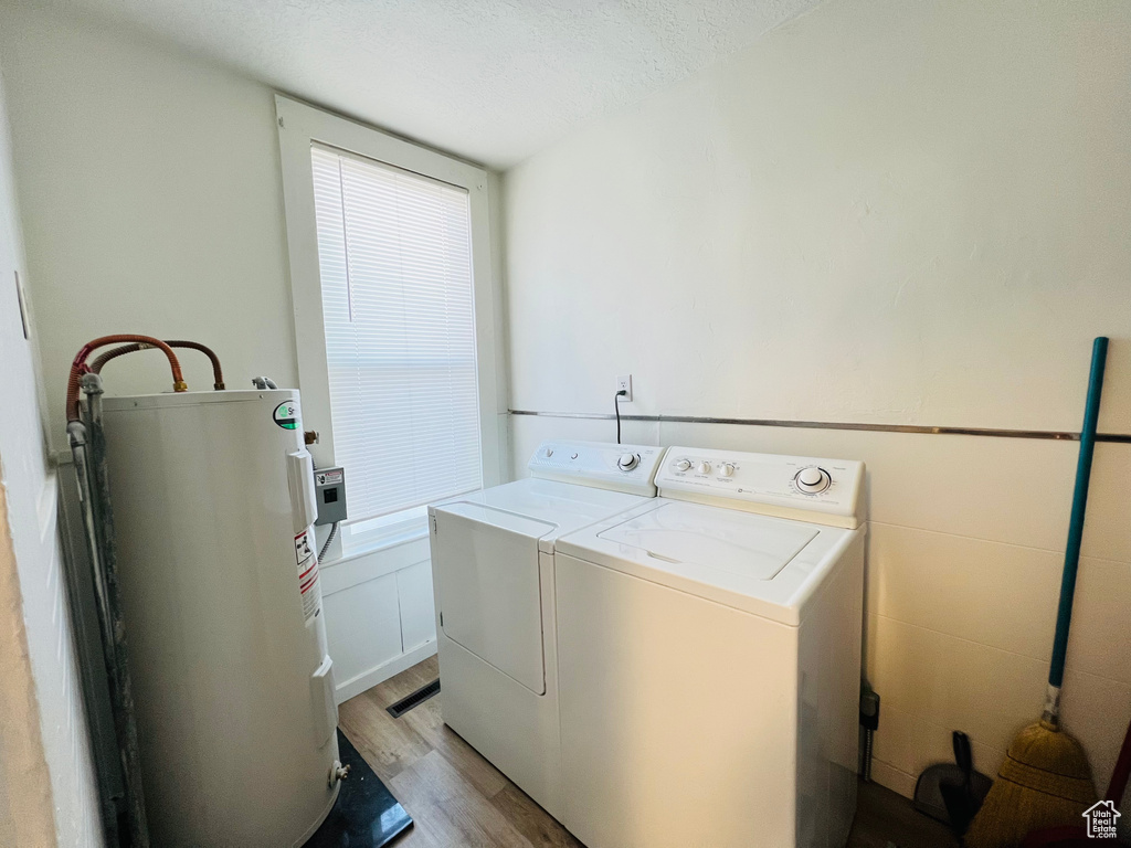 Washroom with a textured ceiling, electric water heater, light hardwood / wood-style floors, and washer and clothes dryer