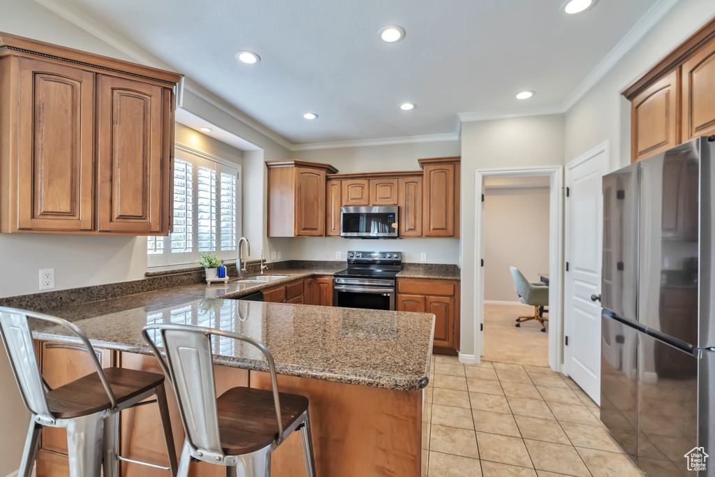 Kitchen featuring light tile floors, stainless steel appliances, ornamental molding, sink, and a kitchen bar