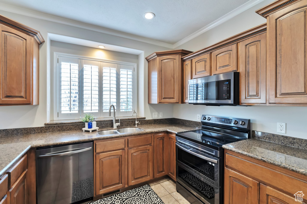 Kitchen with appliances with stainless steel finishes, light tile floors, crown molding, sink, and dark stone counters