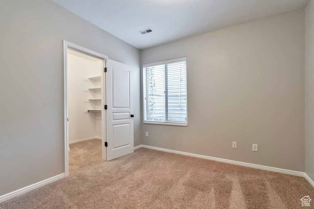 Unfurnished bedroom featuring a walk in closet, light carpet, and a closet