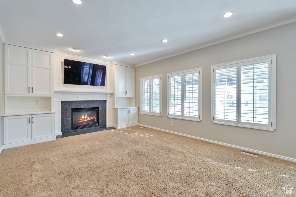 Unfurnished living room featuring light colored carpet, a high end fireplace, and crown molding