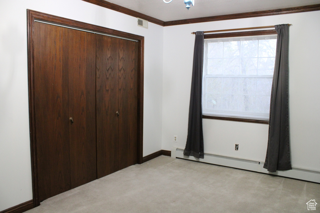 Unfurnished bedroom featuring light colored carpet, baseboard heating, a closet, and crown molding