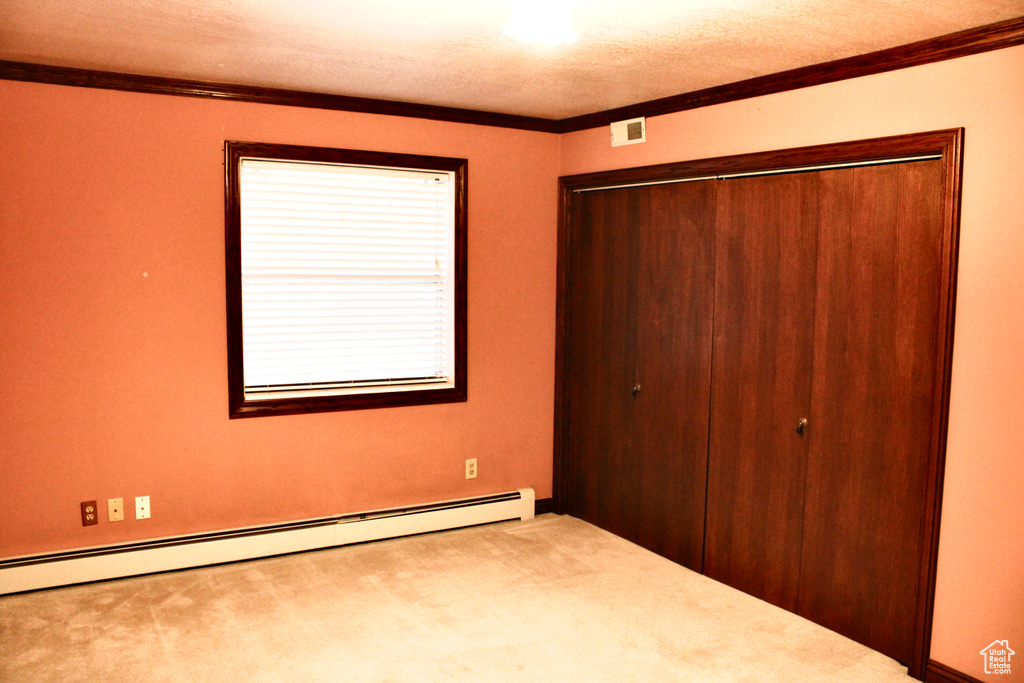 Unfurnished bedroom with carpet flooring, crown molding, a baseboard heating unit, and a closet