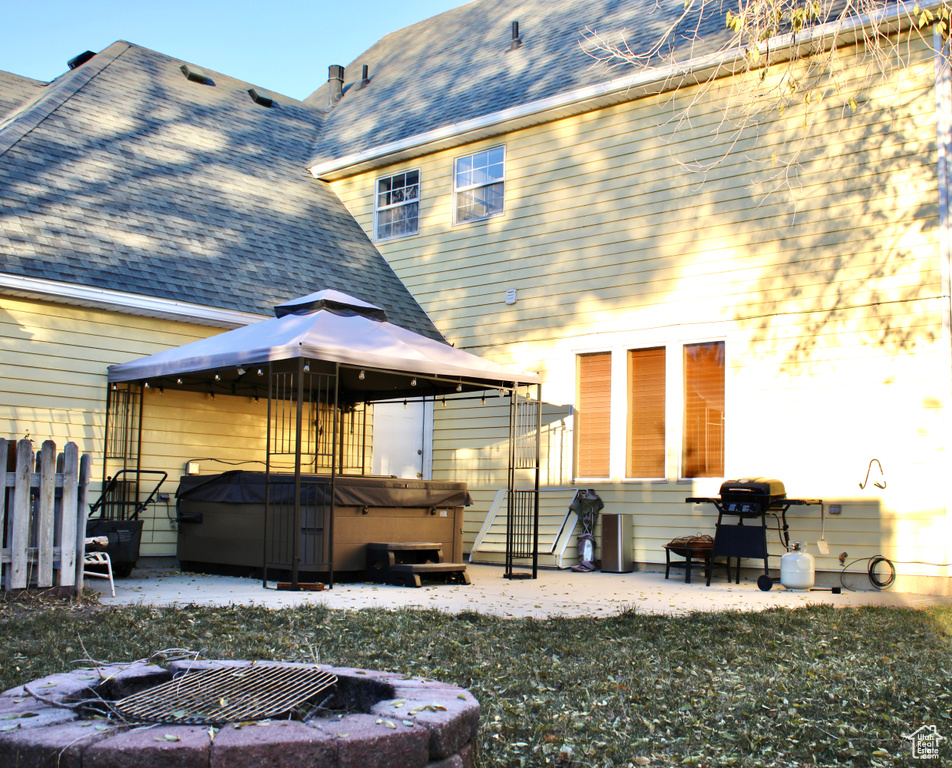 Back of house with a hot tub, a gazebo, and an outdoor fire pit