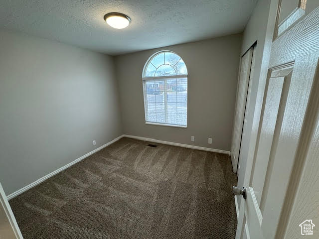 Unfurnished room with a textured ceiling and dark colored carpet