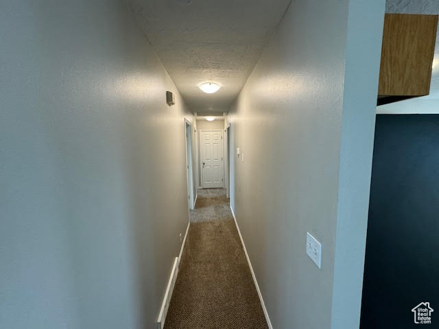 Hallway with dark colored carpet and a textured ceiling
