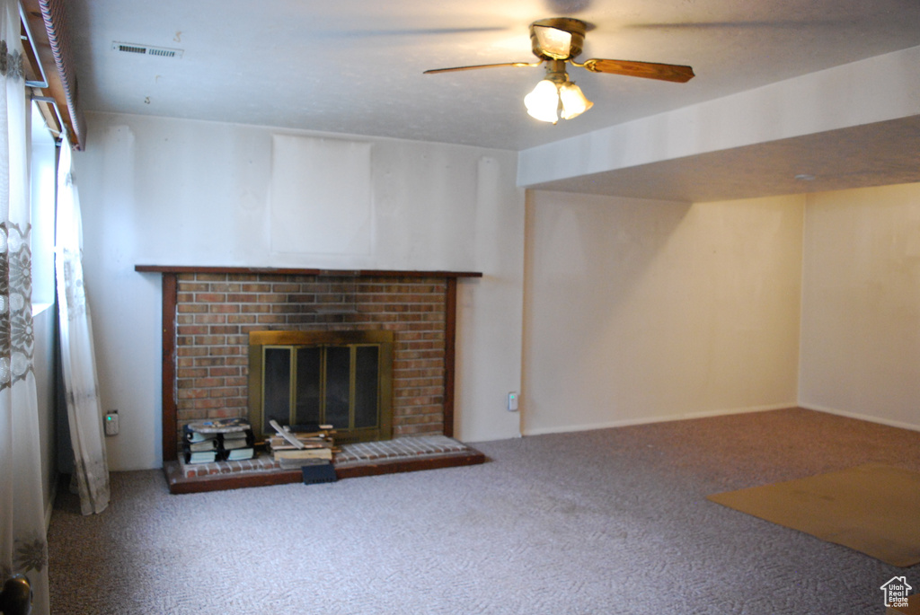 Unfurnished living room featuring a brick fireplace, carpet floors, and ceiling fan