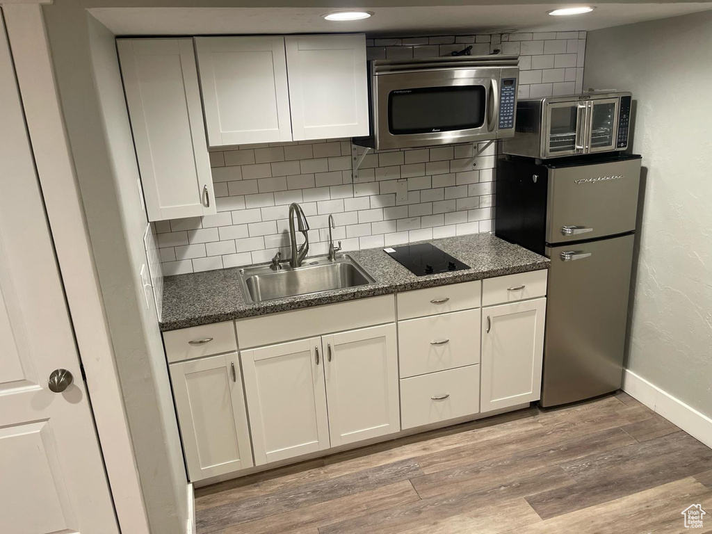 Kitchen with white cabinetry, light hardwood / wood-style flooring, and backsplash