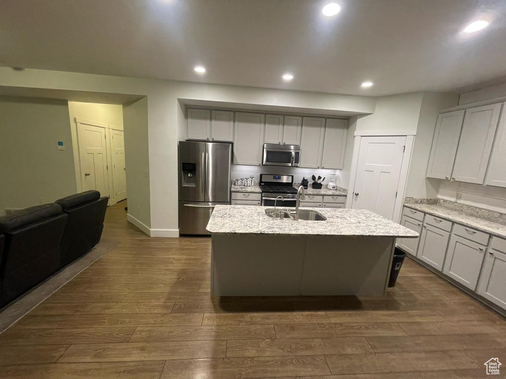 Kitchen with dark hardwood / wood-style flooring, sink, light stone countertops, a kitchen island with sink, and appliances with stainless steel finishes