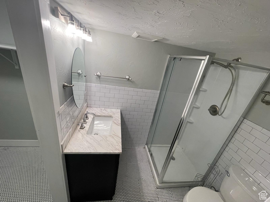 Bathroom with tile walls, a shower with shower door, tile floors, vanity, and toilet