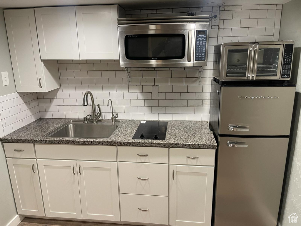 Kitchen featuring sink, white cabinets, fridge, black electric stovetop, and backsplash