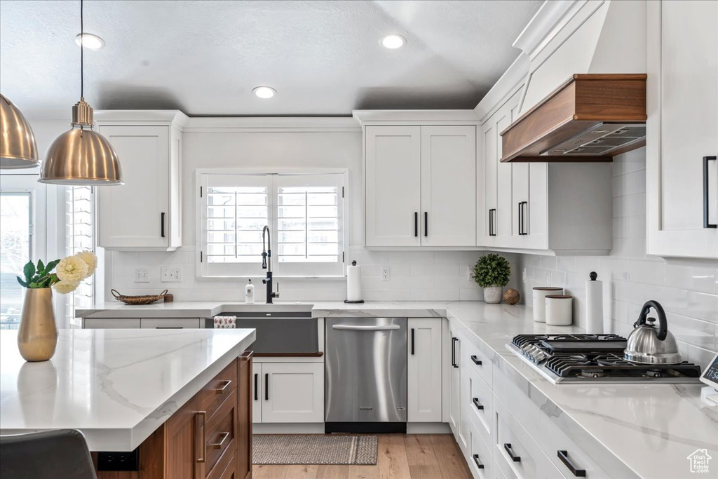 Kitchen featuring hanging light fixtures, tasteful backsplash, white cabinets, and light hardwood / wood-style flooring