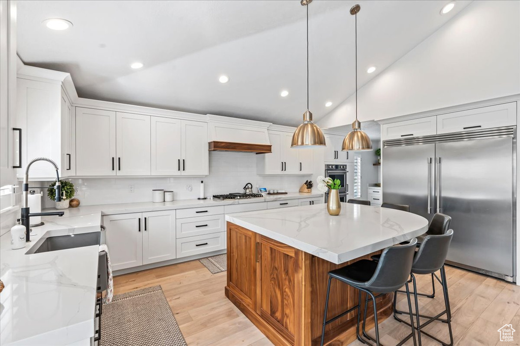 Kitchen with a center island, pendant lighting, light hardwood / wood-style floors, backsplash, and stainless steel appliances