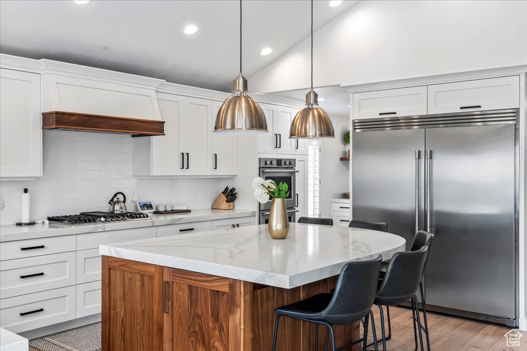 Kitchen featuring appliances with stainless steel finishes, vaulted ceiling, light hardwood / wood-style floors, and a kitchen island