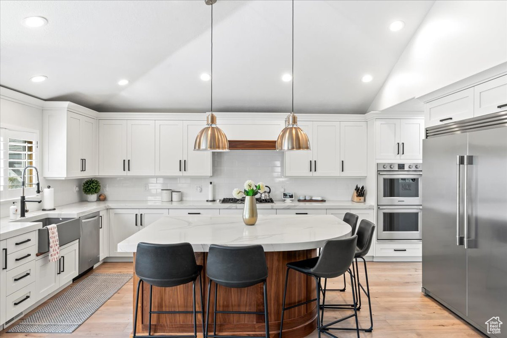 Kitchen featuring stainless steel appliances, vaulted ceiling, a center island, and light hardwood / wood-style flooring