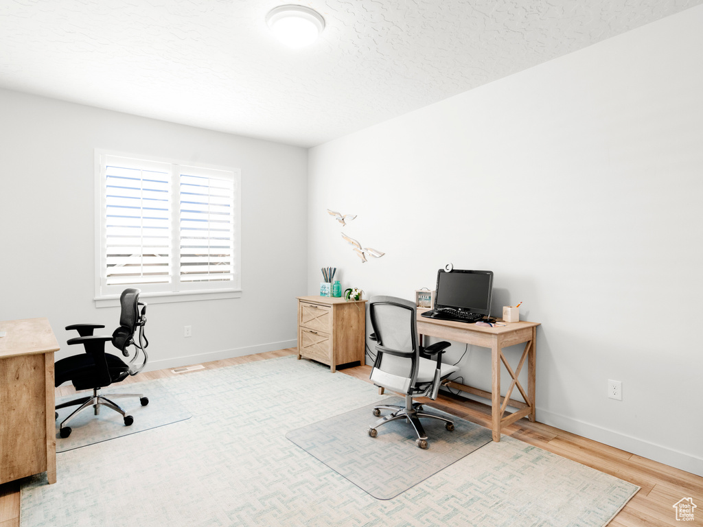 Office with light hardwood / wood-style flooring and a textured ceiling